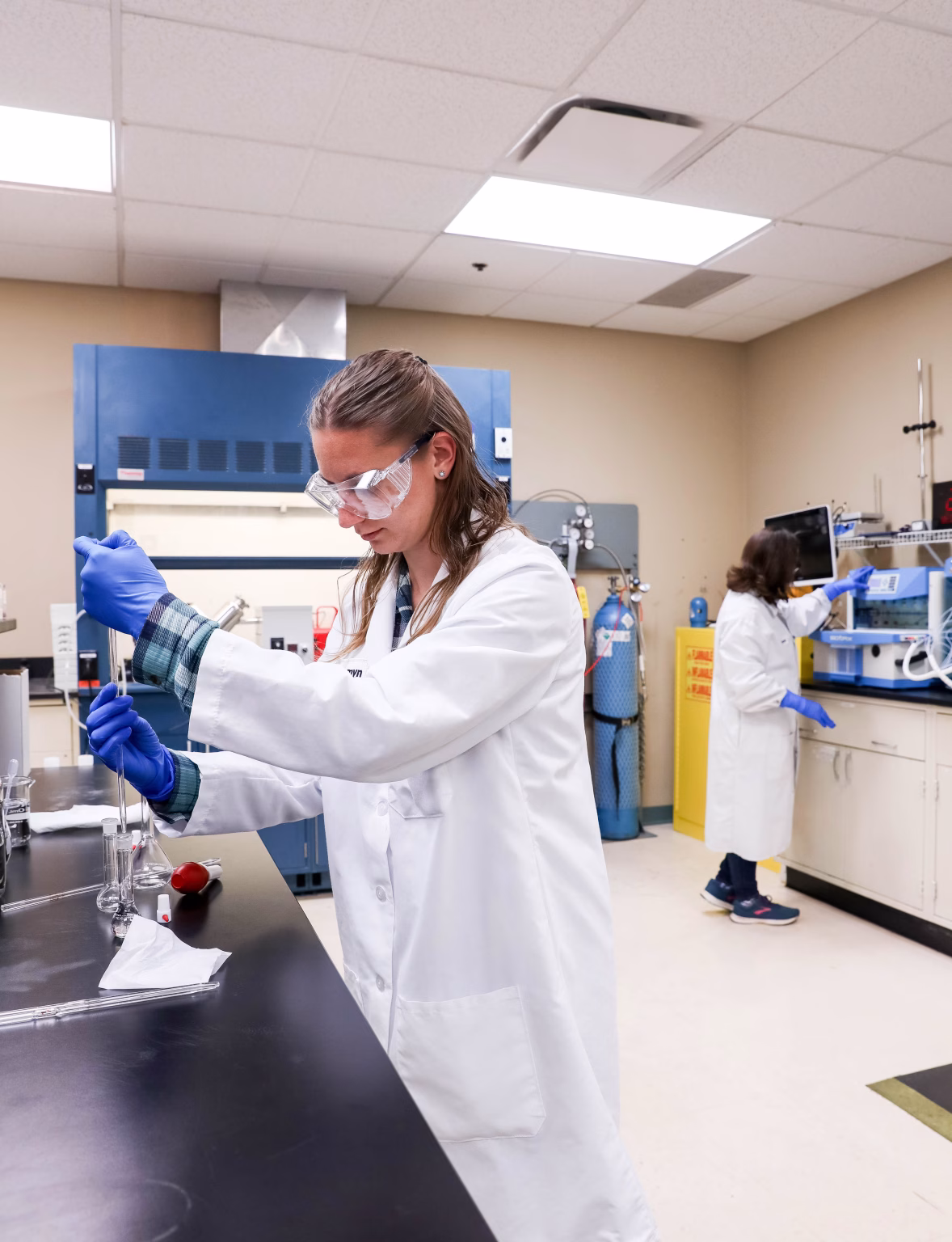 CMC Scientist in GMP laboratory performing drug formulation activities with another chemist in the background